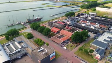 Lelystad, Flevoland, Hollanda - 09.06.2025: Limanı, renkli binaları ve su boyunca yanaşmış bir taklit gemisi olan kıyı kasabasının havadan görünüşü. Çevredeki alanlar park alanlarını içeriyor