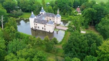 Uçsuz bucaksız yeşil tarlaları, dolambaçlı su yolları ve Hollanda 'nın düz kırsalında parçalı bulutlu bir gökyüzünün altında uzanan bir nehirle çevrili tarihi bir şatonun havadan görünüşü..