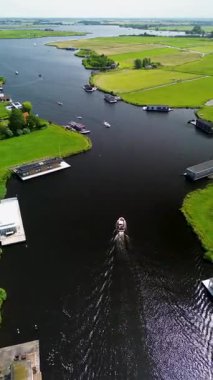 Yüzen evler ve yeşil tarlalarla kaplı huzurlu bir nehirde küçük bir tekne geziniyor. Hava görüntüsü sakin suyu, canlı manzarayı ve sakin kırsal atmosferi yakalar..