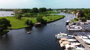 Warmond, Güney Hollanda, Hollanda - 09.06.2025: Ahşap rıhtımlar boyunca kenetlenmiş bir marinanın tepeden aşağı manzarası, yeşil parklarla çevrili dar bir su yolunda seyreden bir tekne