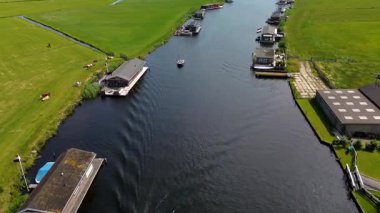 Yüzen evler ve yeşil tarlalarla kaplı huzurlu bir nehirde küçük bir tekne geziniyor. Hava görüntüsü sakin suyu, canlı manzarayı ve sakin kırsal atmosferi yakalar..
