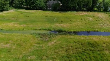Yoğun bir ormanı, büyük tuğlalı bir evi ve yakınlardaki şatoya benzeyen bir binası olan huzurlu bir kırsal alan. Sakin kanalda dinlenen küçük tekneler ve arka planda sessiz bir köy var..