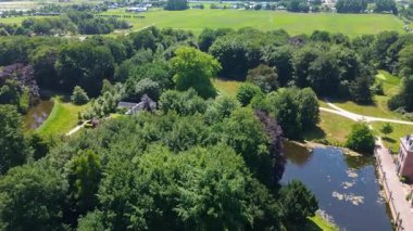 Etrafı yemyeşil ağaçlar, sakin bir gölet ve dolambaçlı yollarla çevrili tarihi bir arazinin manzarası. Huzurlu manzara doğal güzelliği mimari cazibeyle harmanlıyor..