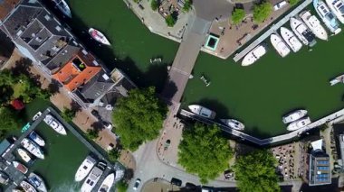 Kenarları teknelerle kenetlenmiş büyüleyici bir kanal manzarası, sudan geçen bir köprü ve yeşil ve kaldırımlı caddelerle çevrili samimi binalar. Huzurlu ve resimli.