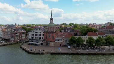 Hollanda nehir kenarı manzaralı bir şehir, tarihi bir mimari sergilenen, uzun bir saat kulesi, kırmızı çatılar, ve dağınık bulutlu parlak bir gökyüzü altında sakin bir rıhtım geçidi.