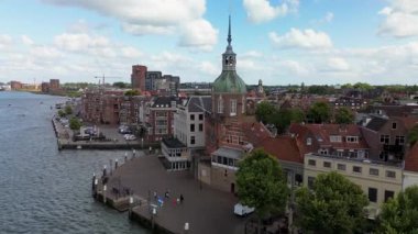 Hollanda nehir kenarı manzaralı bir şehir, tarihi bir mimari sergilenen, uzun bir saat kulesi, kırmızı çatılar, ve dağınık bulutlu parlak bir gökyüzü altında sakin bir rıhtım geçidi.