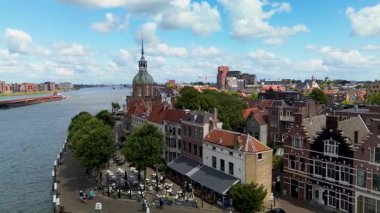 Hollanda nehir kenarı manzaralı bir şehir, tarihi bir mimari sergilenen, uzun bir saat kulesi, kırmızı çatılar, ve dağınık bulutlu parlak bir gökyüzü altında sakin bir rıhtım geçidi.