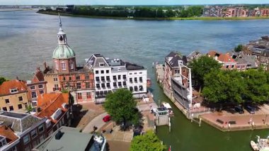 Hollanda nehir kenarı manzaralı tarihi kubbeli bir bina, kırmızı kiremitli çatılar, asma köprü ve yeşil bir kanal boyunca kenetlenmiş tekneler..