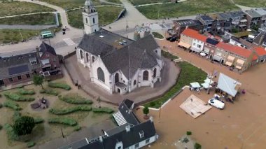 Hollanda 'nın kıyı kasabasının sokakları, arabaları ve manzaralı yeşillikleriyle çevrili eşsiz geometrik çatısı olan kaleye benzeyen tarihi bir kilisenin tepeden aşağı insansız hava aracı görüntüsü. Kırmızı kiremitli güzel evler.