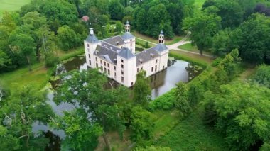Uçsuz bucaksız yeşil tarlaları, dolambaçlı su yolları ve Hollanda 'nın düz kırsalında parçalı bulutlu bir gökyüzünün altında uzanan bir nehirle çevrili tarihi bir şatonun havadan görünüşü..