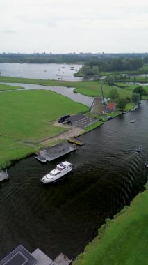 Yüzen evler ve yeşil tarlalarla kaplı huzurlu bir nehirde küçük bir tekne geziniyor. Hava görüntüsü sakin suyu, canlı manzarayı ve sakin kırsal atmosferi yakalar..