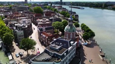 Kubbeli bir kulesi, geleneksel binaları, ağaçlarla kaplı caddeleri ve bulutlu bir gökyüzünün altında geniş bir nehirde yelken açan bir teknesi olan tarihi bir Avrupa şehri manzarası..