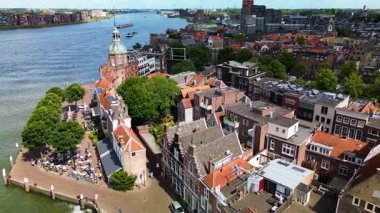 Hollanda nehir kenarı manzaralı tarihi kubbeli bir bina, kırmızı kiremitli çatılar, asma köprü ve yeşil bir kanal boyunca kenetlenmiş tekneler..