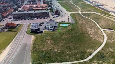 Hollanda kıyı kasabasının üzerinde gün batımı manzarası. Kırmızı çatılı evler, ağaçlarla kaplı sokaklar ve ufukta görünen deniz, altın ışığın altında..