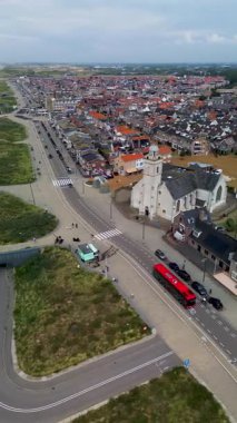 Kırmızı çatılı evleri olan bir sahil kasabasının havadan görünüşü, tarihi bir kilise, kum tepeleri boyunca kıvrılan yollar, ve kıyı şeridi boyunca şemsiyeler ve plaj kulübeleriyle kaplı geniş kumlu bir sahil..