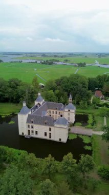 Uçsuz bucaksız yeşil tarlaları, dolambaçlı su yolları ve Hollanda 'nın düz kırsalında parçalı bulutlu bir gökyüzünün altında uzanan bir nehirle çevrili tarihi bir şatonun havadan görünüşü..