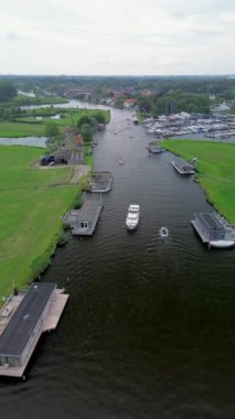 Uçsuz bucaksız yeşil çayırlar ve Hollanda bayraklarıyla kesişen, bulutlu bir gökyüzünün altında rüzgarda hafifçe sallanan su yollarıyla çevrili, nehirde yüzen evlerin sakin bir görüntüsü. Klasik bir Hollanda yel değirmeni