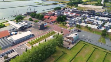 Lelystad, Flevoland, Hollanda - 09.06.2025: Limanı, renkli binaları ve su boyunca yanaşmış bir taklit gemisi olan kıyı kasabasının havadan görünüşü. Çevredeki alanlar park alanlarını içeriyor