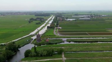 Yeşil alanlar ve kanallarla çevrili klasik bir Hollanda yel değirmeninin hava görüntüleri. Geleneksel Hollanda kırsalını yukarıdan gösteren barışçıl bir kırsal bölge..