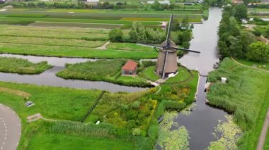 Yeşil alanlar ve kanallarla çevrili klasik bir Hollanda yel değirmeninin hava görüntüleri. Geleneksel Hollanda kırsalını yukarıdan gösteren barışçıl bir kırsal bölge..