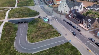 Kumlu bir sahilin havadan görünüşü. İnsanlar sığ gel-git havuzları ve kum havuzlarının yanında yürüyor. Denizden hafif dalgalar yaklaşıyor..