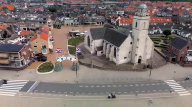Kumlu bir sahilin havadan görünüşü. İnsanlar sığ gel-git havuzları ve kum havuzlarının yanında yürüyor. Denizden hafif dalgalar yaklaşıyor..