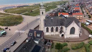 Kumlu bir sahilin havadan görünüşü. İnsanlar sığ gel-git havuzları ve kum havuzlarının yanında yürüyor. Denizden hafif dalgalar yaklaşıyor..