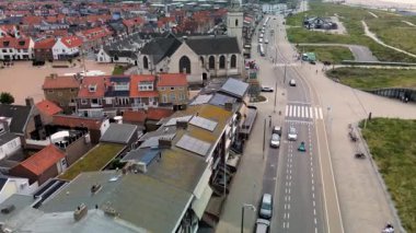 Kumlu bir sahilin havadan görünüşü. İnsanlar sığ gel-git havuzları ve kum havuzlarının yanında yürüyor. Denizden hafif dalgalar yaklaşıyor..