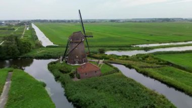 Yeşil alanlar ve kanallarla çevrili klasik bir Hollanda yel değirmeninin hava görüntüleri. Geleneksel Hollanda kırsalını yukarıdan gösteren barışçıl bir kırsal bölge..