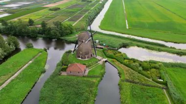 Yeşil alanlar ve kanallarla çevrili klasik bir Hollanda yel değirmeninin hava görüntüleri. Geleneksel Hollanda kırsalını yukarıdan gösteren barışçıl bir kırsal bölge..