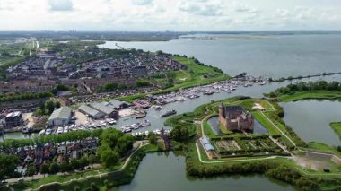 Hollanda 'daki Muiderslot Kalesi' nin göz kamaştırıcı hava manzarası, kanallarla çevrili, tekne dolu bir marina ve ufka doğru uzanan büyüleyici bir kasaba manzarası..