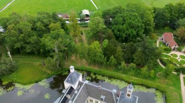 Uçsuz bucaksız yeşil tarlaları, dolambaçlı su yolları ve Hollanda 'nın düz kırsalında parçalı bulutlu bir gökyüzünün altında uzanan bir nehirle çevrili tarihi bir şatonun havadan görünüşü..