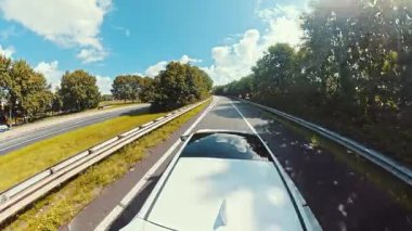 Parlak mavi gökyüzünün altında, huzurlu ve ağaçlarla kaplı bir otoyol boyunca güneşli bir sürüş, doğayı ve önümüzde uzanan açık yolu rahatlatıcı bir şekilde gösteriyor..