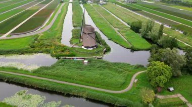 Yeşil alanlar ve kanallarla çevrili klasik bir Hollanda yel değirmeninin hava görüntüleri. Geleneksel Hollanda kırsalını yukarıdan gösteren barışçıl bir kırsal bölge..