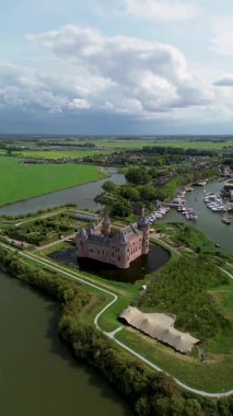 Hollanda 'daki Muiderslot Kalesi' nin göz kamaştırıcı hava manzarası, kanallarla çevrili, tekne dolu bir marina ve ufka doğru uzanan büyüleyici bir kasaba manzarası. Yürüyen yolları olan yeşil alanlar..