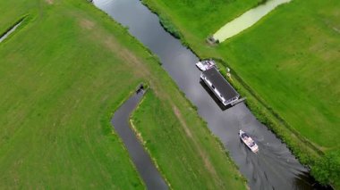 Yeşil tarlaları olan dar bir kanalın havadan görünüşü, demirli bir yüzen ev ve sakin suda seyreden küçük bir motorlu tekne. Yüzen evlerle dolu huzurlu bir nehirde küçük bir tekne geziniyor..