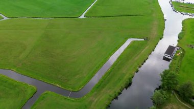 Yeşil tarlaların sarmal kanallarla bölünmüş havadan görünüşü, küçük bir rıhtımlı yüzen ev ve kıyıya demirli tekneler. Yeşil tarlalı dar bir kanalın havadan görünüşü, demirli bir yüzen ev..