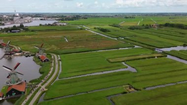 Nehir boyunca Zaanse Schans 'ta yeşil tarlalar, kanallar ve turistlerle çevrili geleneksel Hollanda yel değirmenlerinin insansız hava aracı görüntüsü. Nehir kenarındaki Hollanda yel değirmenleri.