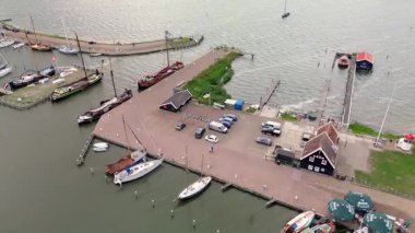 Bulutlu bir günde yelkenli, balıkçı tekneleri, park alanı ve kurtarma istasyonunun bulunduğu küçük bir limanın havadan görüntüsü..
