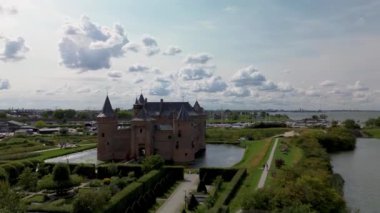 Hollanda 'daki Muiderslot Kalesi' nin göz kamaştırıcı hava manzarası, kanallarla çevrili, tekne dolu bir marina ve ufka doğru uzanan büyüleyici bir kasaba manzarası. Yürüyen yolları olan yeşil alanlar..