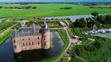 Hollanda 'daki Muiderslot Kalesi' nin göz kamaştırıcı hava manzarası, kanallarla çevrili, tekne dolu bir marina ve ufka doğru uzanan büyüleyici bir kasaba manzarası. Yürüyen yolları olan yeşil alanlar..
