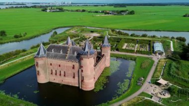 Hollanda 'daki Muiderslot Kalesi' nin göz kamaştırıcı hava manzarası, kanallarla çevrili, tekne dolu bir marina ve ufka doğru uzanan büyüleyici bir kasaba manzarası. Yürüyen yolları olan yeşil alanlar..