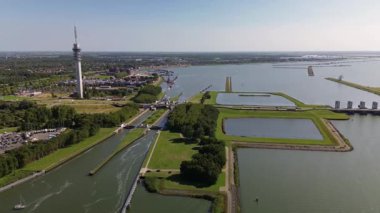 Yüksek bir iletişim kulesi nehir kenti üzerinde yükselmekte, kanallar, köprüler, botlar ve yeşil manzaralarla modern altyapıyı doğal çevreyle harmanlamaktadır..