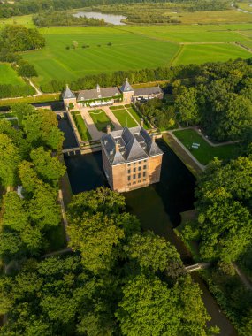 Bahçeleri, köprüsü ve çevresi ağaçlar, su hatları ve sıcak güneş ışığı altındaki yakınlardaki bir köyle çevrili tarihi kale manzarası..