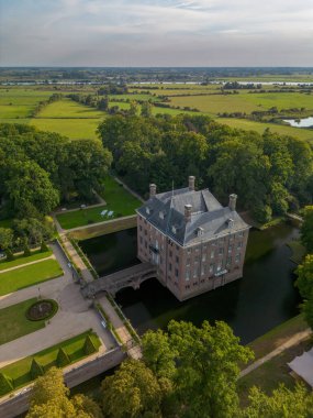 Bahçeleri, köprüsü ve çevresi ağaçlar, su hatları ve sıcak güneş ışığı altındaki yakınlardaki bir köyle çevrili tarihi kale manzarası..