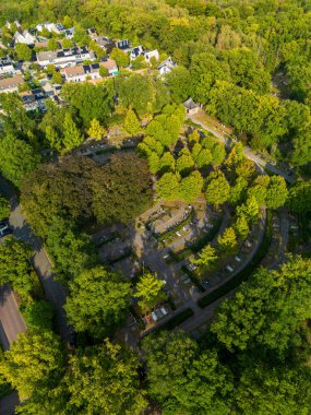 Yoğun ormanlarla çevrili kavisli mezarlık sıralarının hava manzarası, merkezde ve yakınlardaki konut evleri, doğa ve insan tasarımı karışımı..