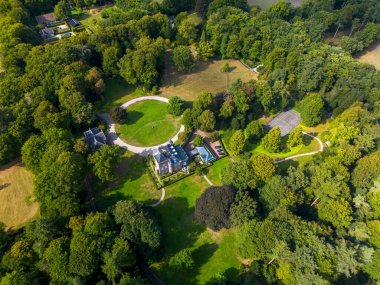 Merkezi malikanesi, yüzme havuzu, tenis kortu, kıvrımlı yollar ve tenha ve yemyeşil ile çevrili bitişik binaların havadan görünüşü..