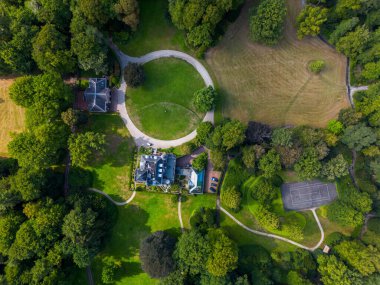 Merkezi malikanesi, yüzme havuzu, tenis kortu, kıvrımlı yollar ve tenha ve yemyeşil ile çevrili bitişik binaların havadan görünüşü..