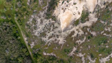 Kumlu aşınmış bölge, yeşil bitki örtüsü ve yoğun çalıların arasından geçen düz bir yol ile doğal karşıtlığı ve arazi kullanımını vurgulayan karışık arazinin havadan görünüşü.
