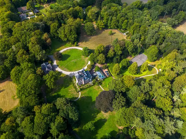 Merkezi malikanesi, yüzme havuzu, tenis kortu, kıvrımlı yollar ve tenha ve yemyeşil ile çevrili bitişik binaların havadan görünüşü..